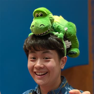 Thomas wearing a blue shirt and posing his hands like a T-rex while wearing a Rex (from Toy Story) headband.
